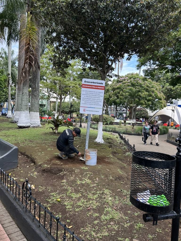 Persona del equipo de TOMATO sembrando junto al rótulo Área arborizada en un parque de Alajuela
