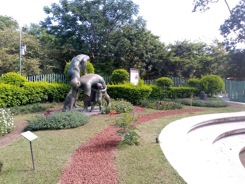 Jardín de esculturas con setos, flores y senderos de piedra roja en el Museo de Arte Costarricense
